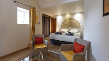 A modern hotel room with a bed, two armchairs, a glass coffee table, and a large window.