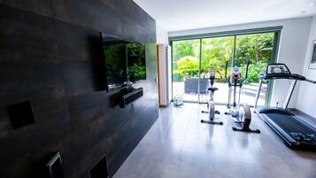 Un gimnasio moderno en casa con un televisor grande, equipo de ejercicio y vistas al exterior con zonas verdes.