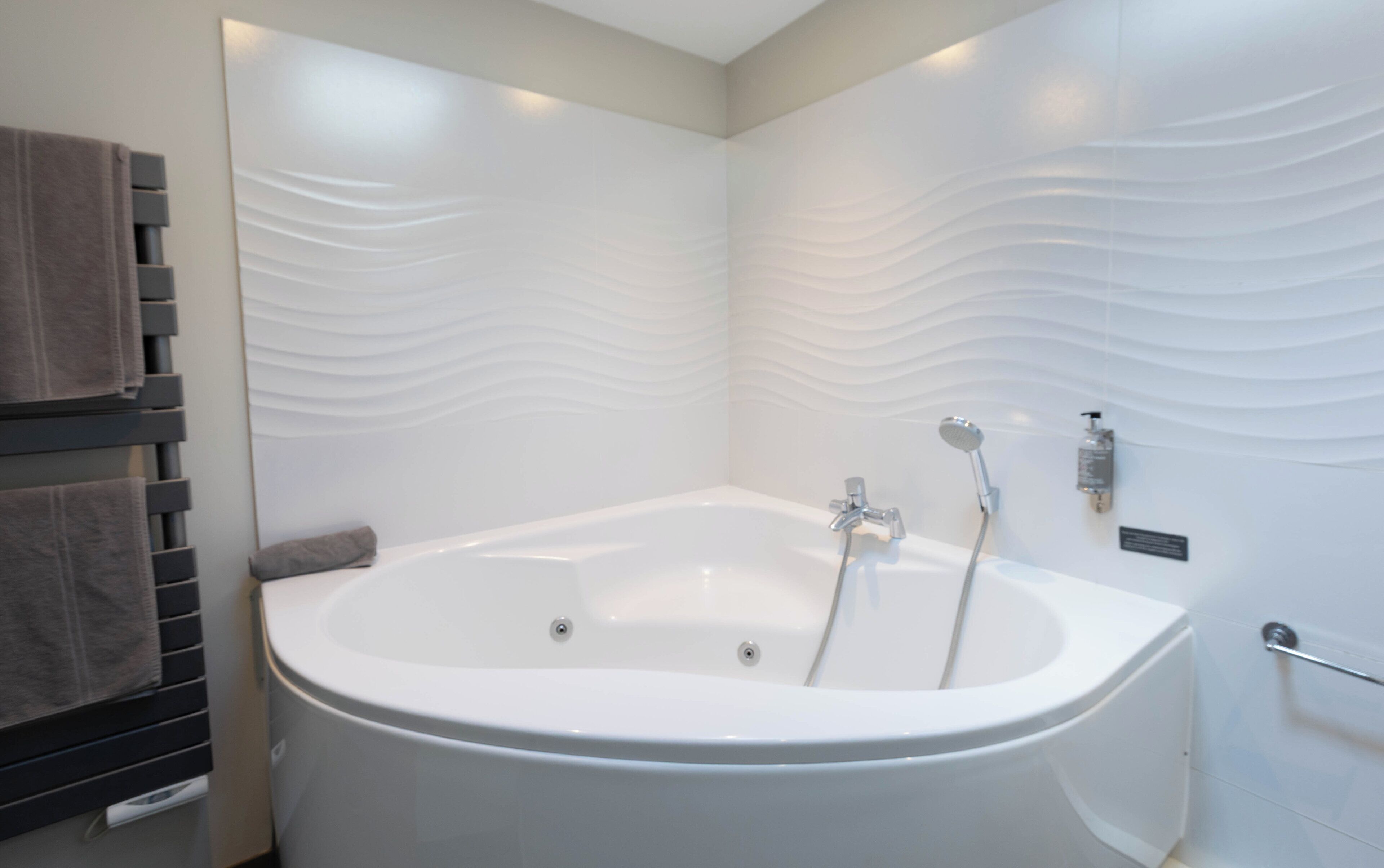 A modern bathroom with a freestanding bathtub, a towel rack, and a wall-mounted soap dispenser.