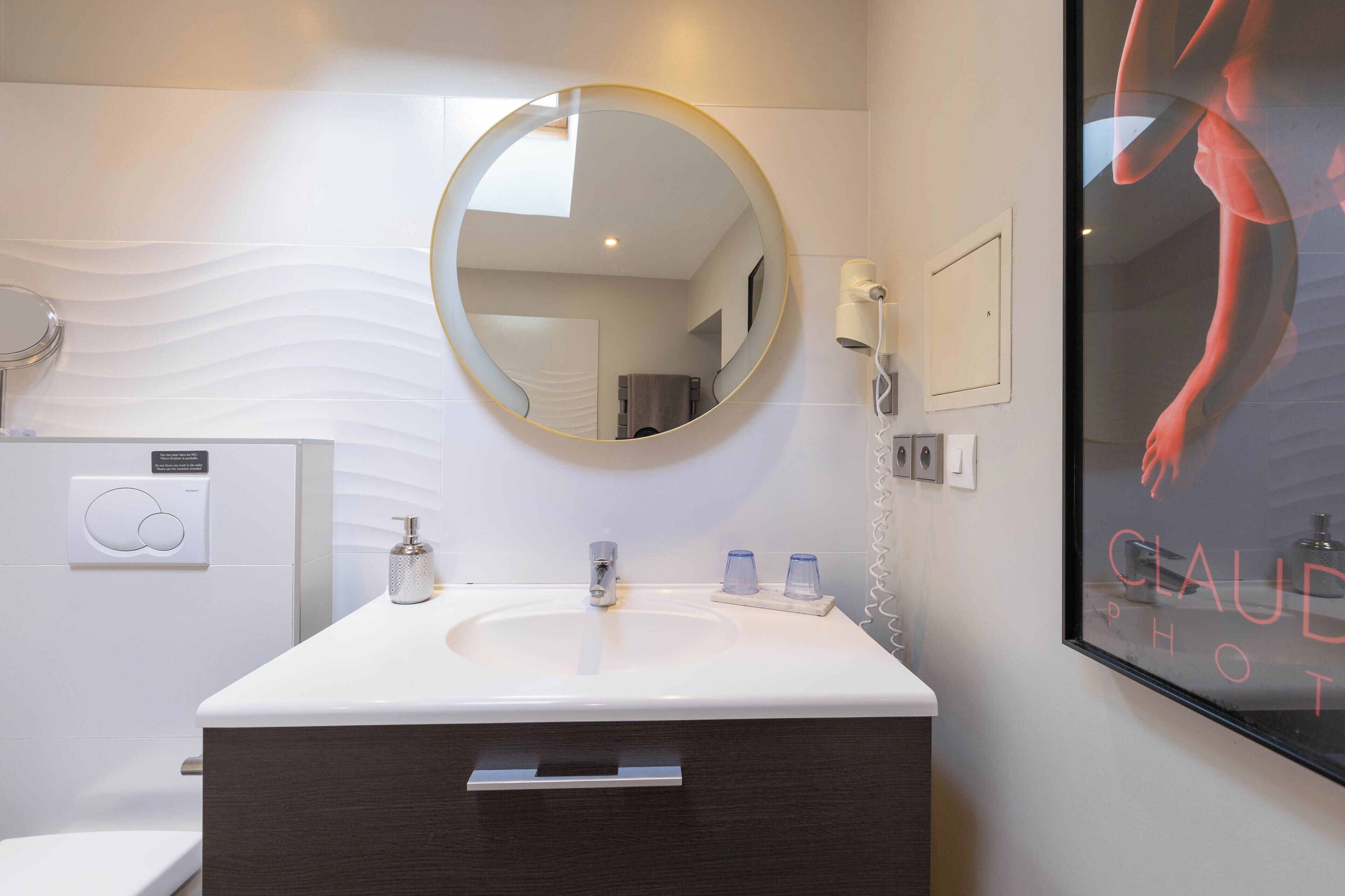 A modern bathroom with a round mirror, a white sink, a towel rack, and a poster on the wall.