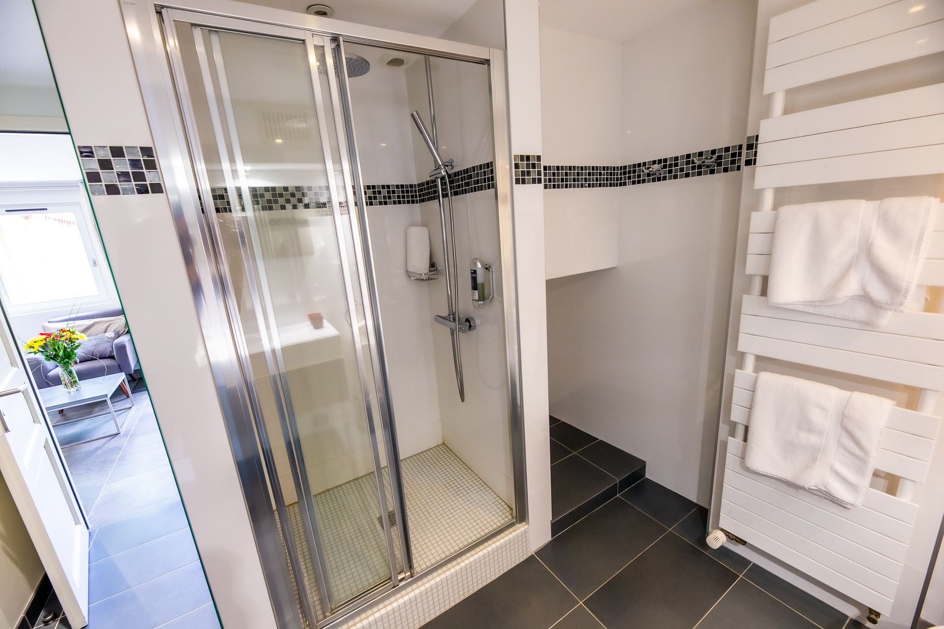 Een moderne badkamer met een glazen douchecabine, een witte handdoekhouder en een betegelde vloer.