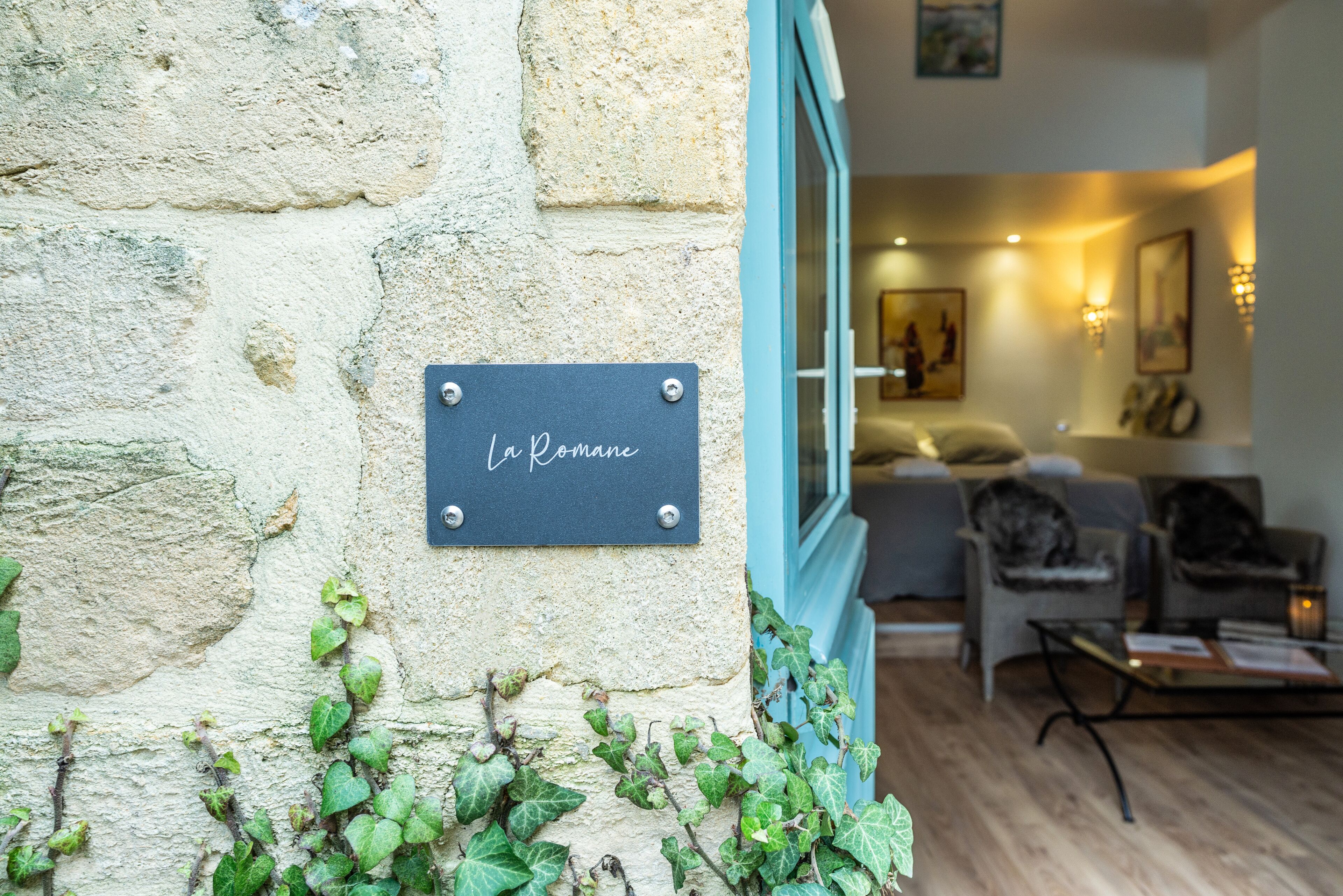 A stone wall with a plaque reading "La Romane" and ivy growing on it.