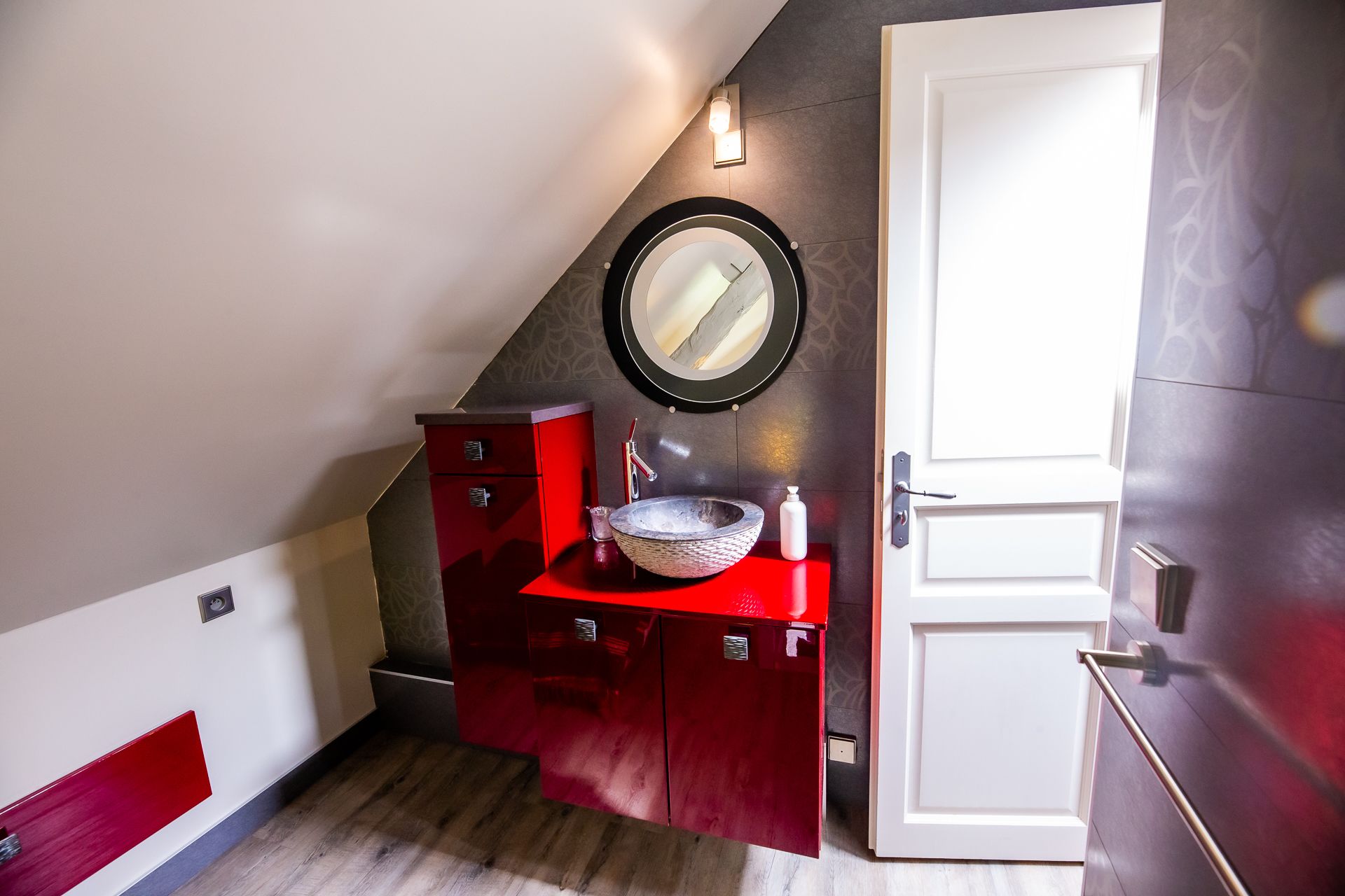 Een badkamer met een rode wastafel, een ronde spiegel en een witte deur.
