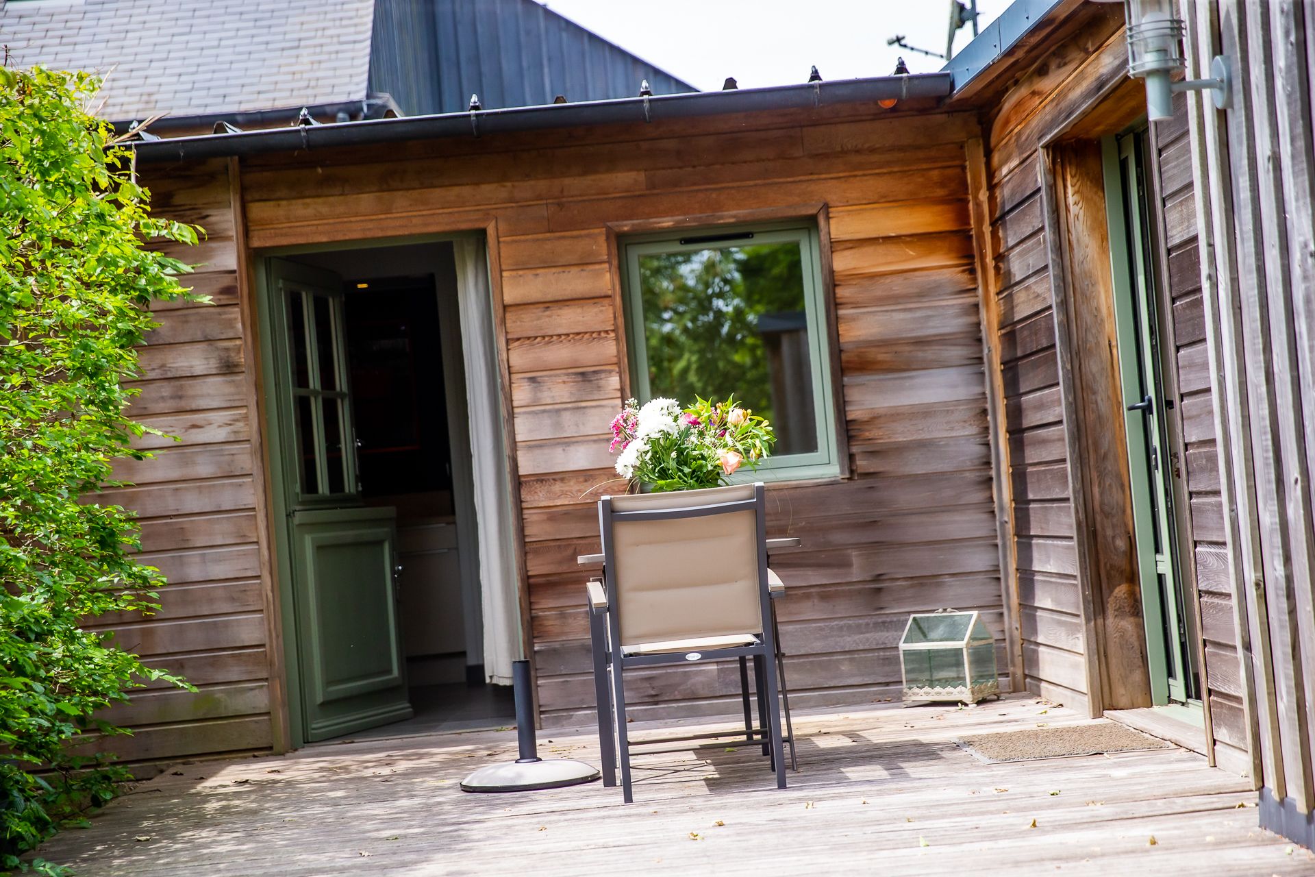 A wooden cabin with a patio, a chair, and a flower vase.
