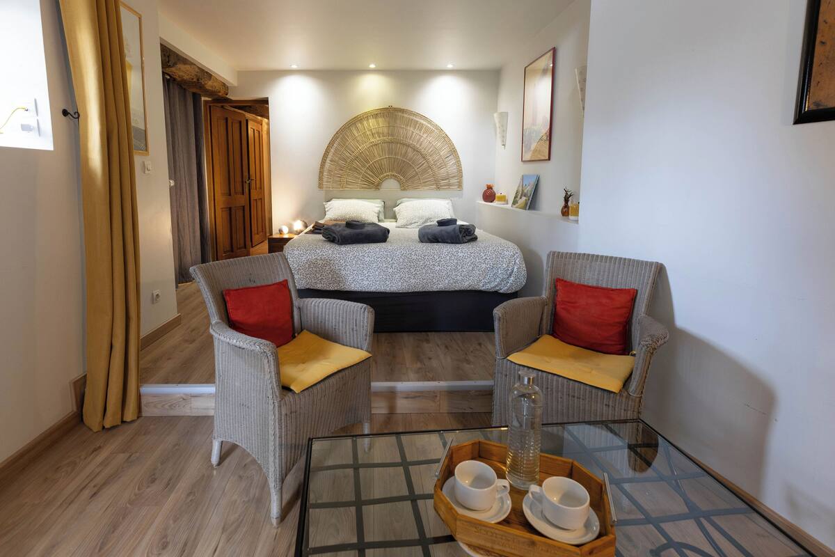 Ein Hotelzimmer mit einem Bett, zwei Sesseln, einem Glastisch und einer Ablage mit Tassen und einer Flasche.