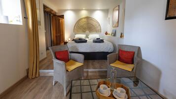 Une chambre d’hôtel avec un lit, deux fauteuils, une table basse en verre et un plateau avec des tasses et une bouteille.
