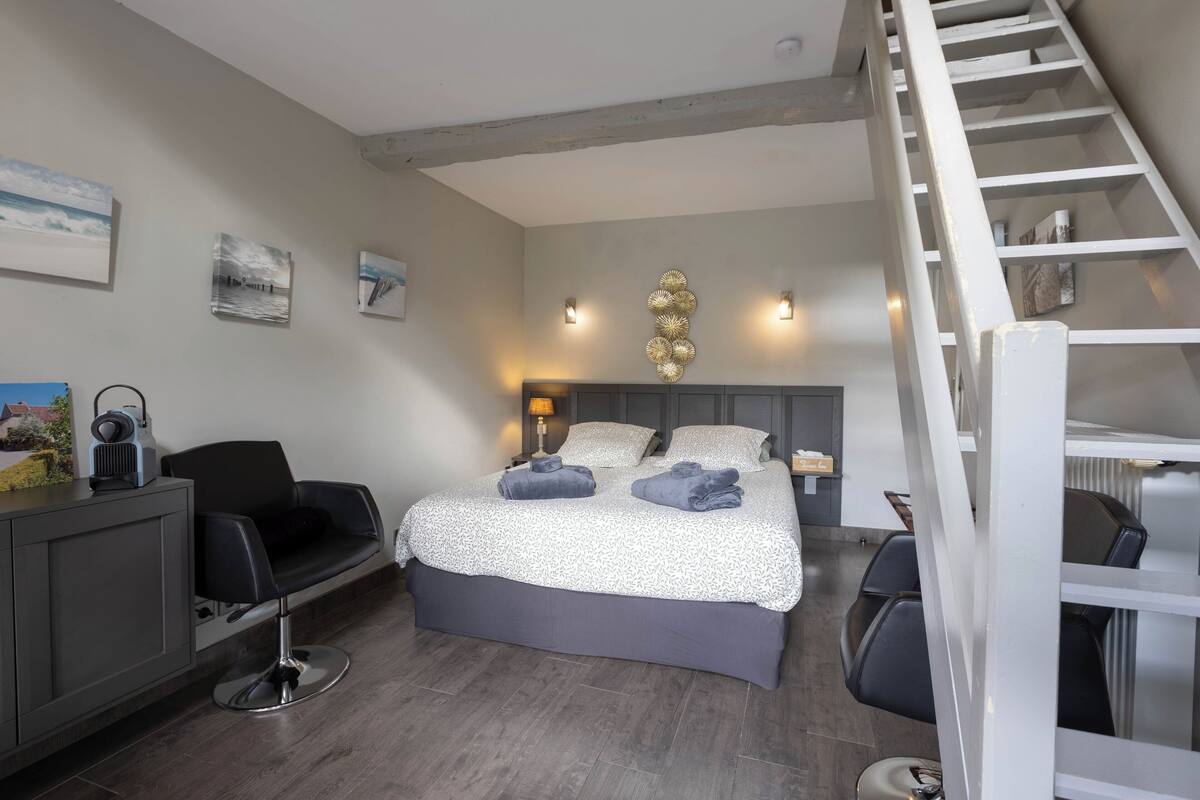 Ein Schlafzimmer mit Bett, Schreibtisch, Stuhl, Lampe und einer Treppe.