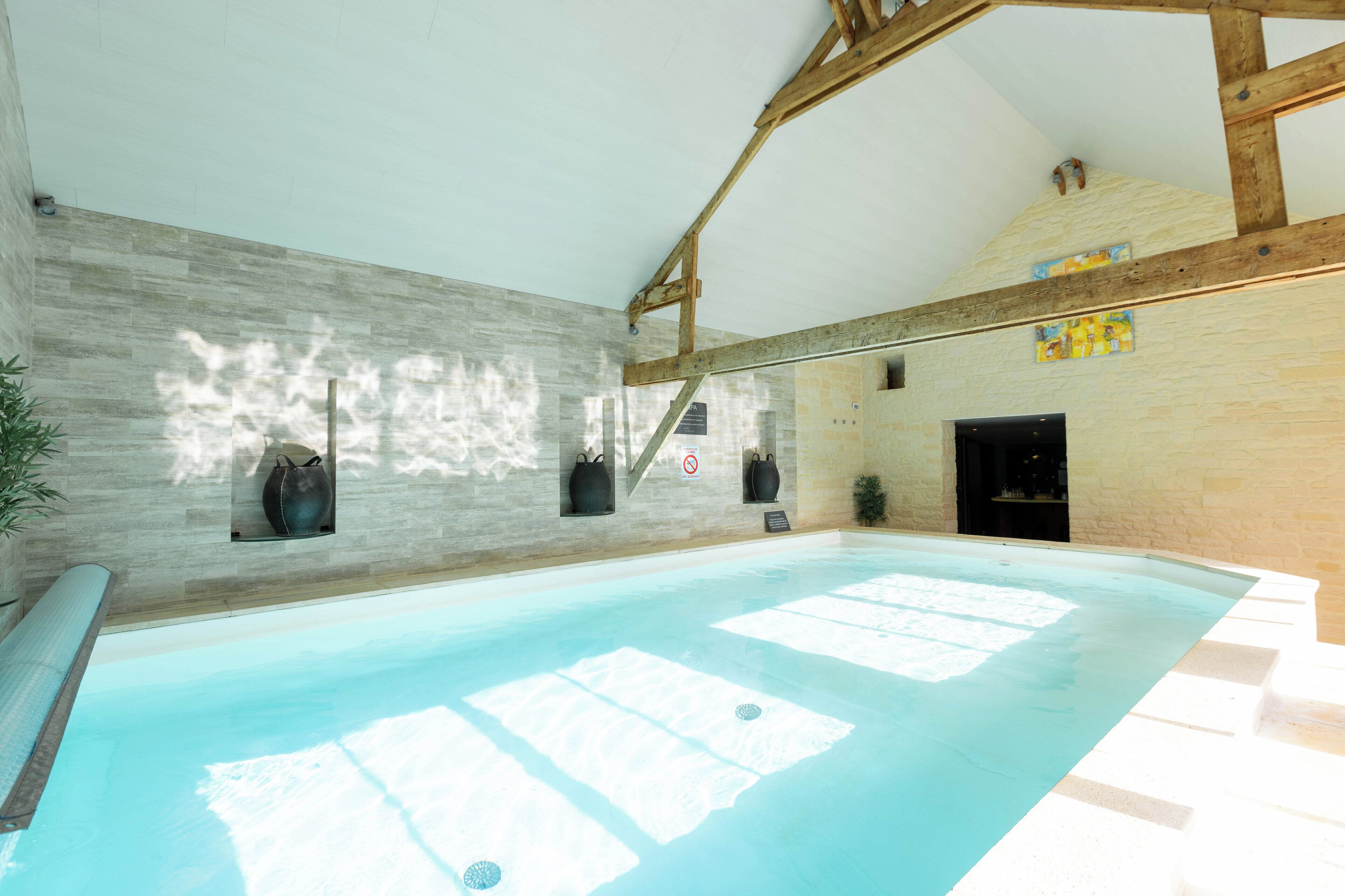 An indoor swimming pool with a stone wall, wooden beams, and a tiled floor.