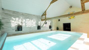 An indoor swimming pool with a stone wall, wooden beams, and a tiled floor.