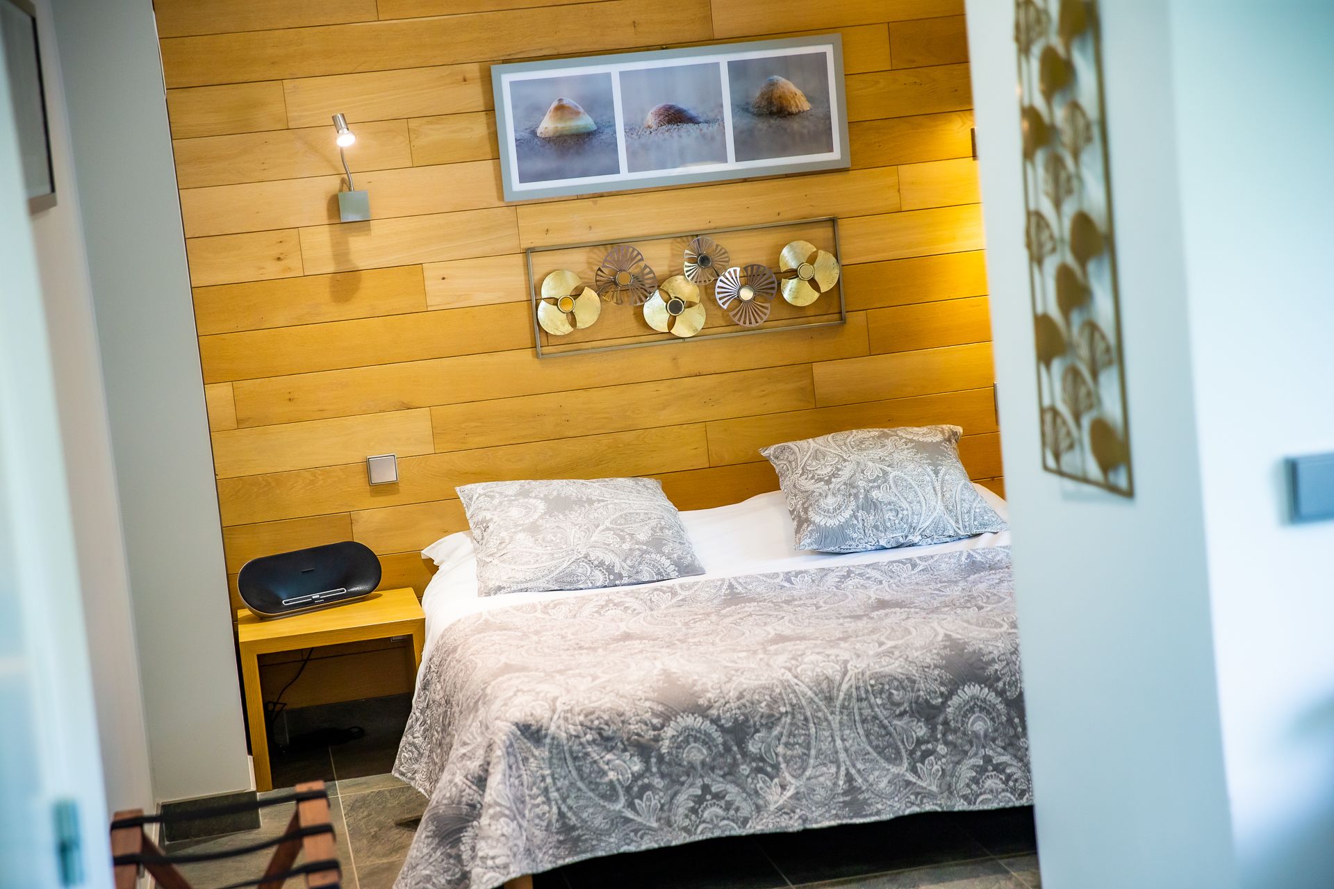 A bedroom with a wooden headboard, a bed with patterned bedding, a bedside table with a lamp, and decorative wall art.