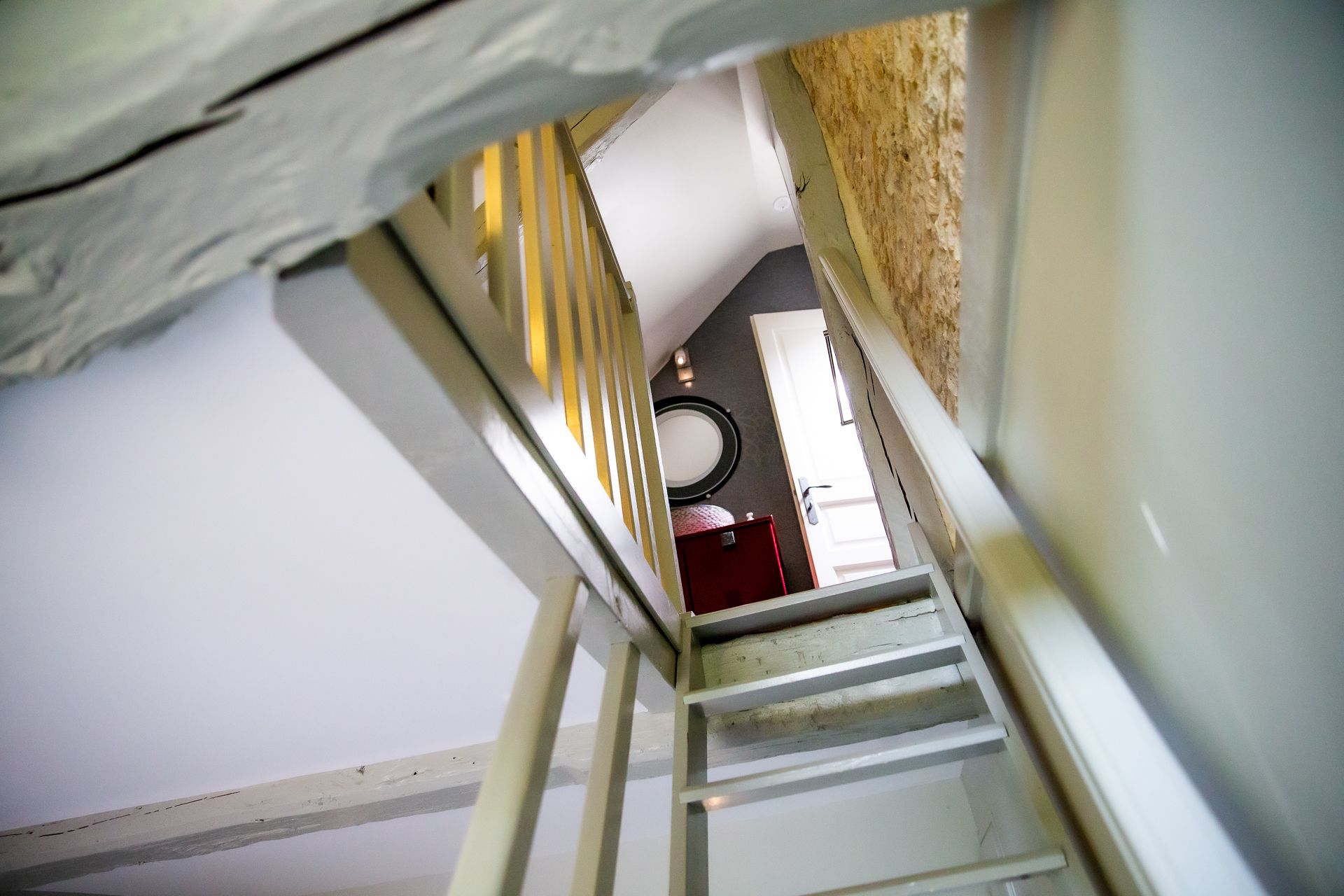 Een trap die leidt naar een kamer met een witte deur, een rode kast en een ronde spiegel aan de muur.