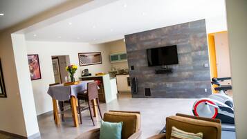 A modern living room with a dining area, a kitchen, and a TV mounted on a stone wall.