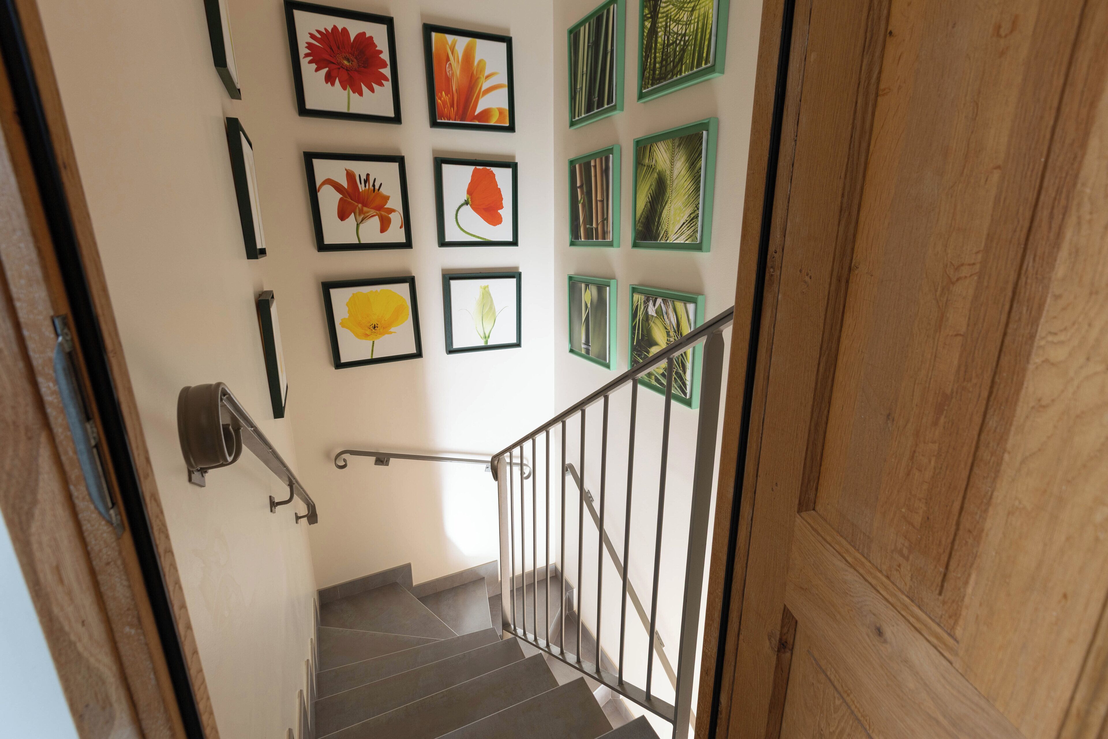 Un escalier avec une rampe en métal, une porte en bois et des œuvres d’art florales encadrées accrochées au mur.