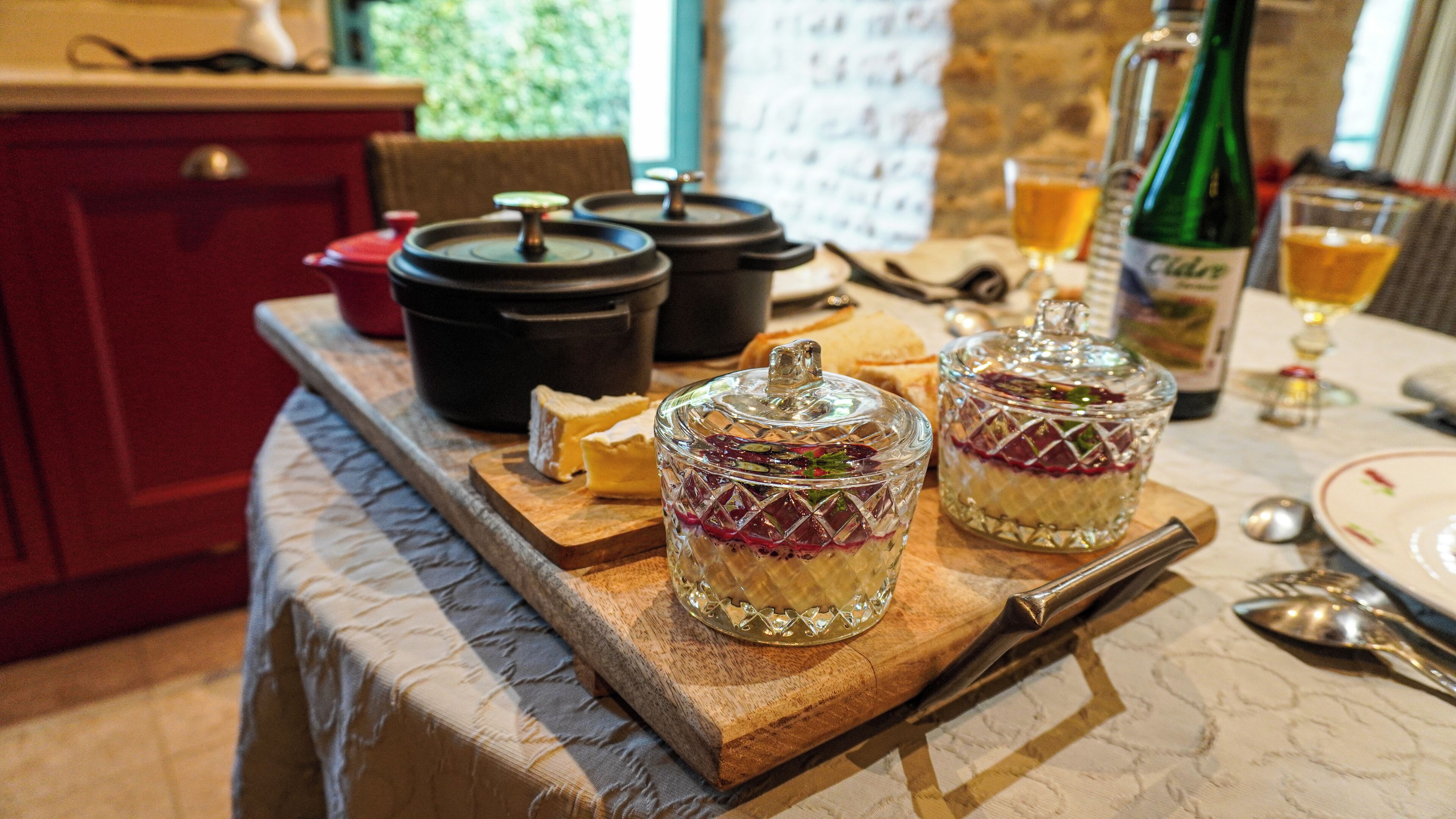 Uma tábua de madeira com dois potes de vidro contendo alimentos em camadas, uma garrafa de vinho e um copo de cerveja sobre uma mesa.