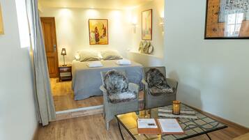 A hotel room with a bed, two chairs, a table, and artwork on the walls.