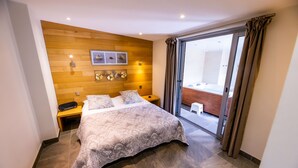 A modern hotel room with a large bed, a wooden headboard, a small bedside table, and a view of the bathroom through a glass door. - Chambres d'Hôtes La Ferme de L'Oudon & Spa (Saint-Pierre-en-Auge)