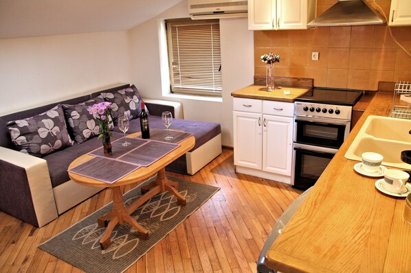 A compact kitchen with a stove, oven, and sink. There's a dining area with a table and a sofa.