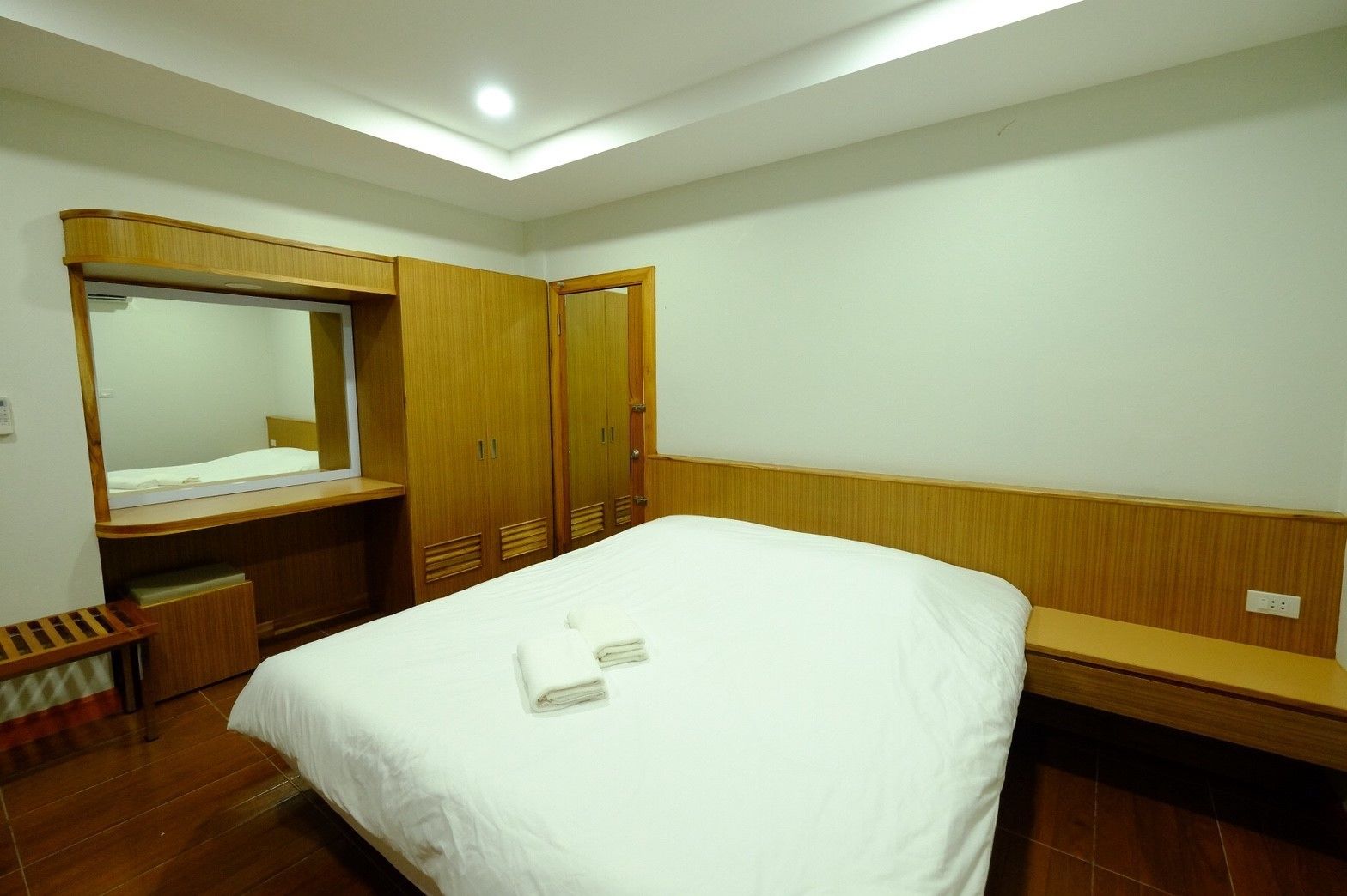 Una habitación de hotel con cama, armario de madera, un espejo y un banco.