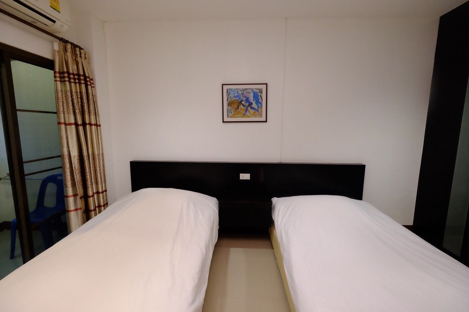 Habitación de hotel con dos camas individuales, un pequeño cuadro en la pared y una ventana con cortinas.
