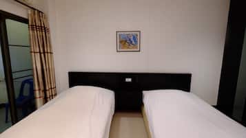 Habitación de hotel con dos camas individuales, un pequeño cuadro en la pared y una ventana con cortinas.
