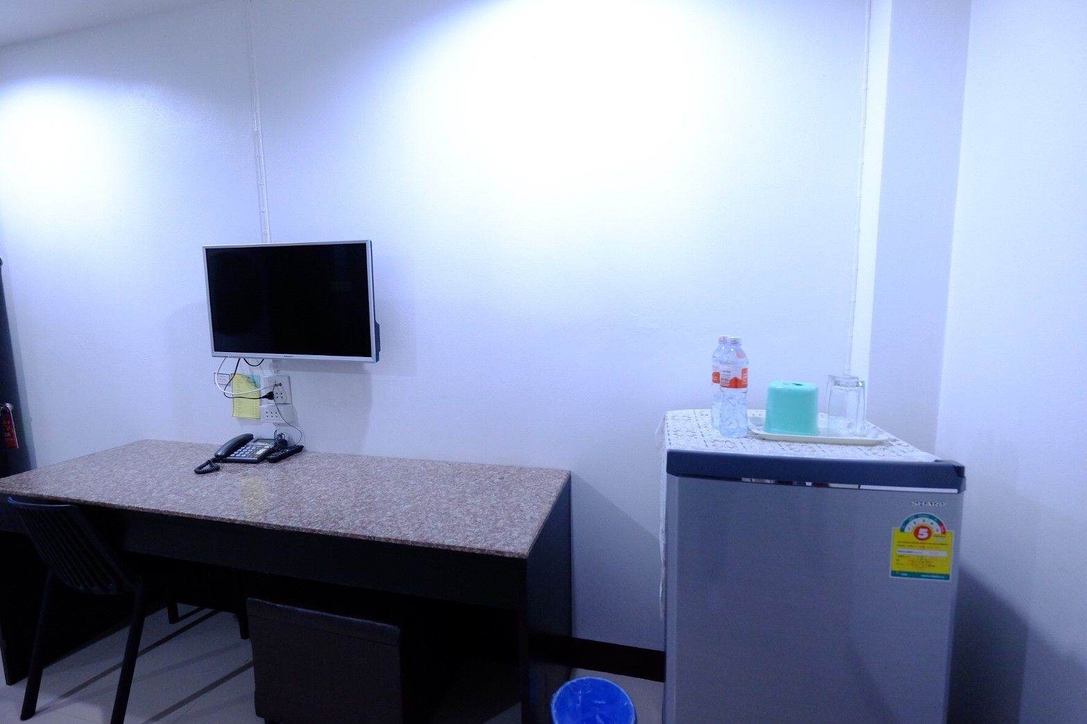 A small office with a desk, chair, a computer monitor, a refrigerator, and a water dispenser.