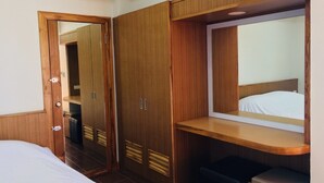 Una habitación de hotel con una cama, un armario, un espejo y un pequeño banco.