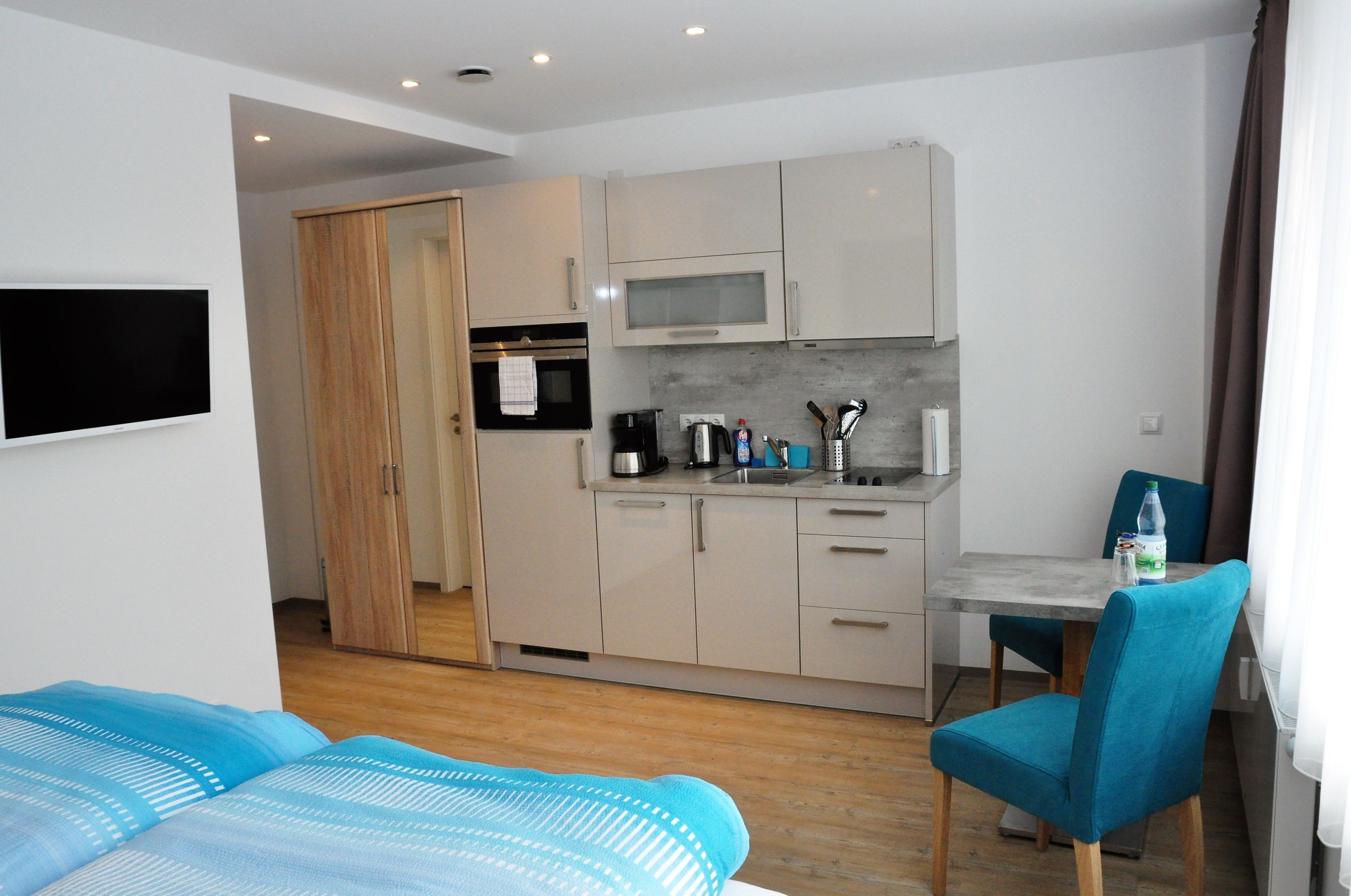 Et moderne hotelværelse med tekøkken, en seng med blåt sengetøj og et spiseområde med bord og stol.