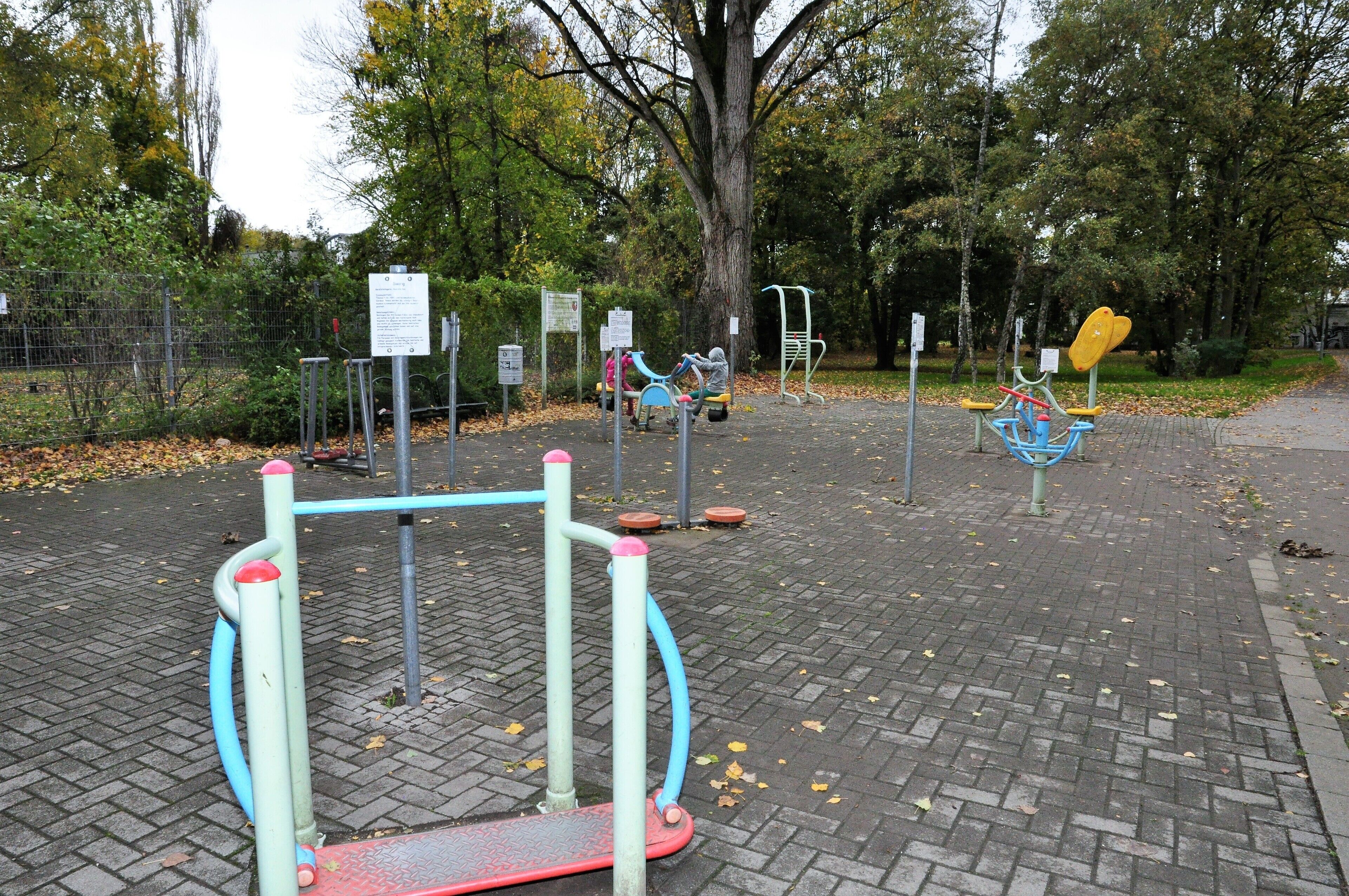 A playground with various exercise equipment, surrounded by trees and a fenced area.