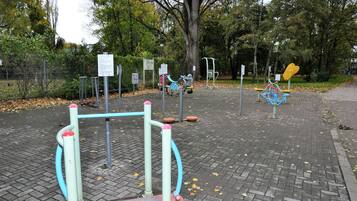 A playground with various exercise equipment, surrounded by trees and a fenced area.