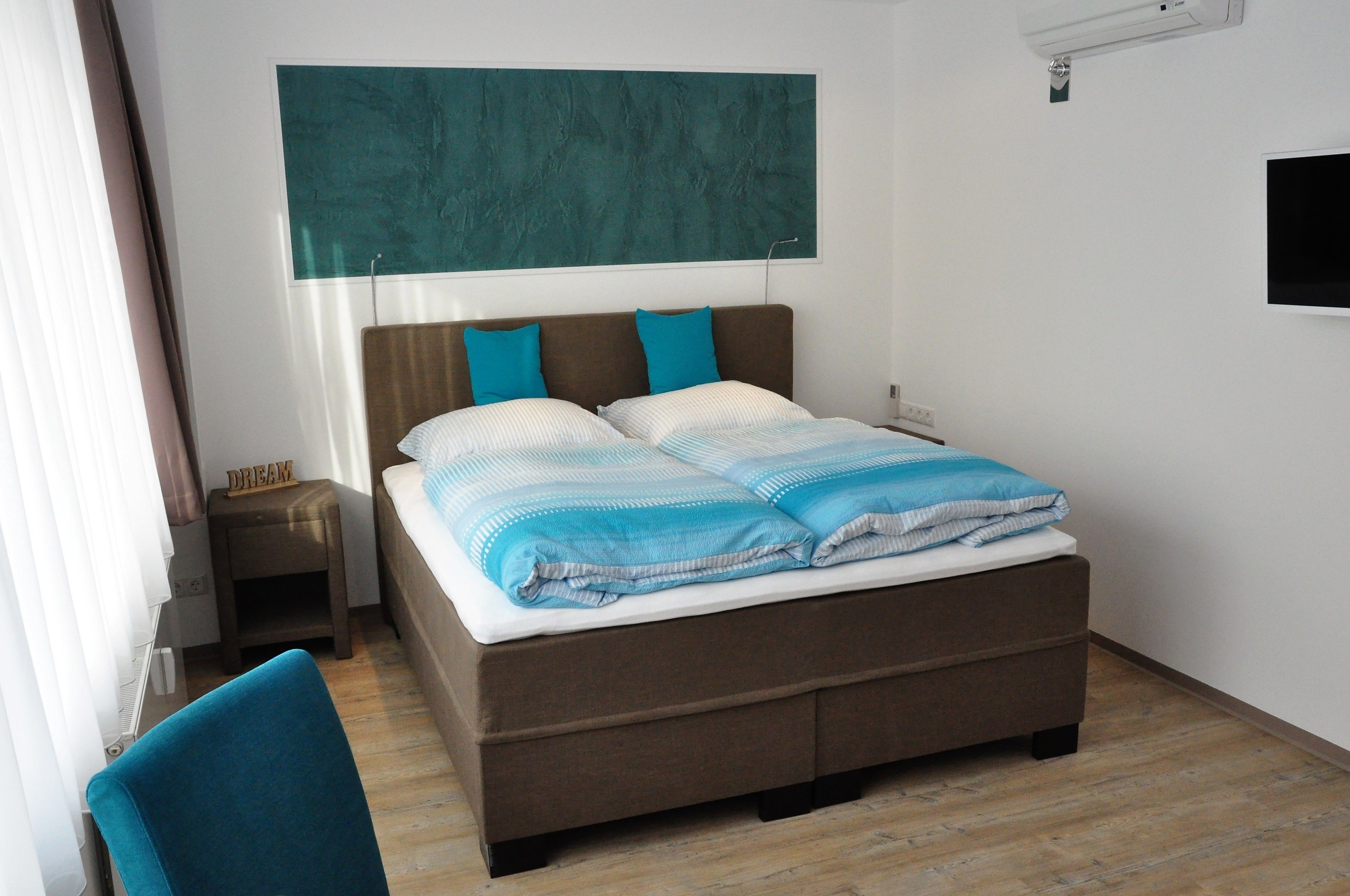 A neatly made bed with a brown headboard, a small bedside table with a lamp, and a wall-mounted TV.