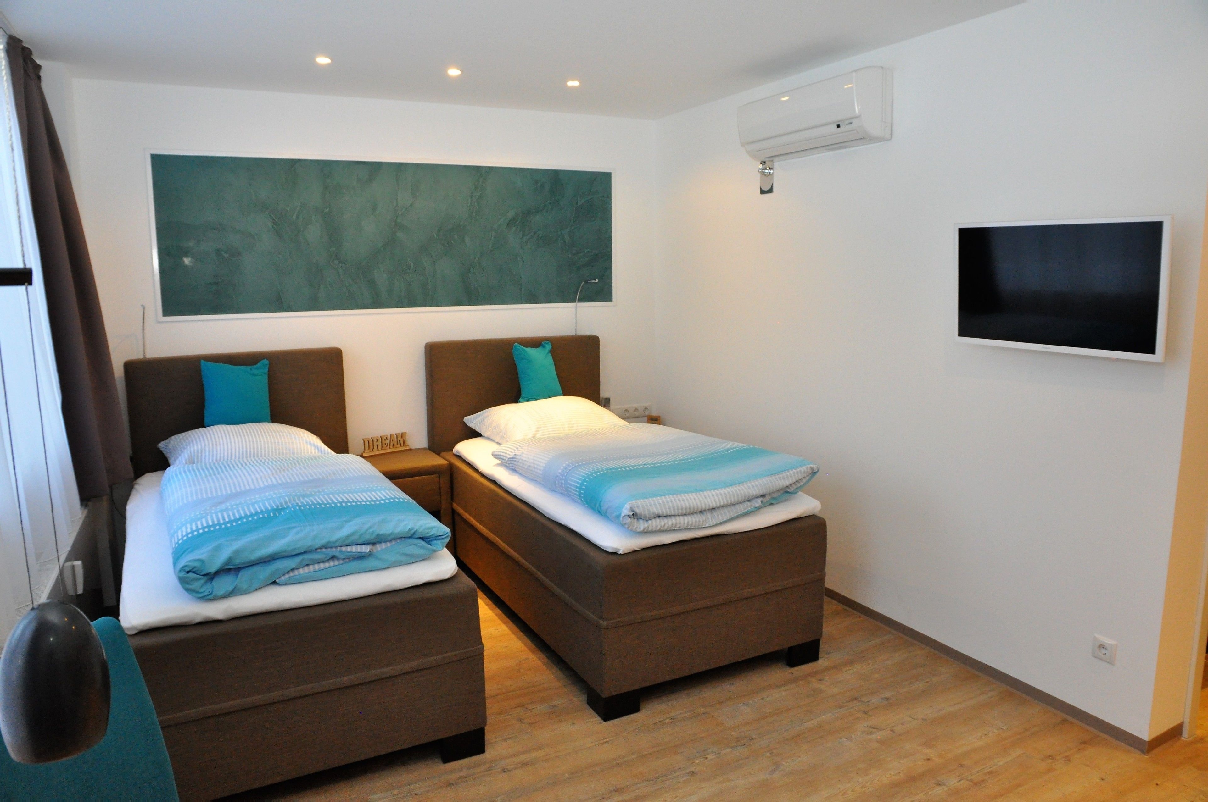 A hotel room with two beds, a large abstract painting, a flat-screen TV, and an air conditioning unit.