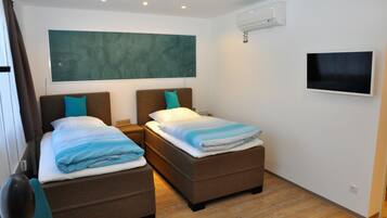 A hotel room with two beds, a large abstract painting, a flat-screen TV, and an air conditioning unit.