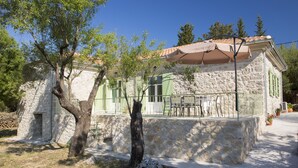 A stone building with a tiled roof, outdoor seating, and a tree in front. - Villa Kodria (Lefkada)