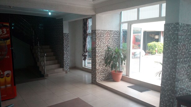 A hotel lobby with a tiled floor, a staircase, a potted plant, and a large window with a view of the outside. - Da 411 Hotel (Ibadan)