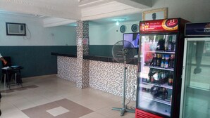A room with a tiled floor, a fan, a refrigerator stocked with beverages, and a clock on the wall. - Da 411 Hotel (Ibadan)