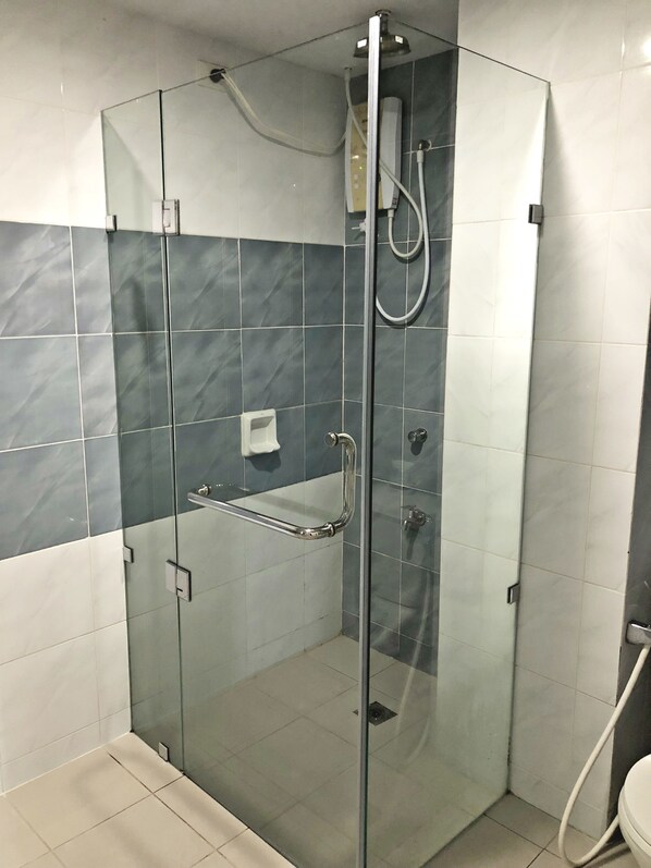 A glass-enclosed shower stall with a handheld showerhead, a glass door, and a white tiled floor. - Ninong's Hotel (Legazpi)