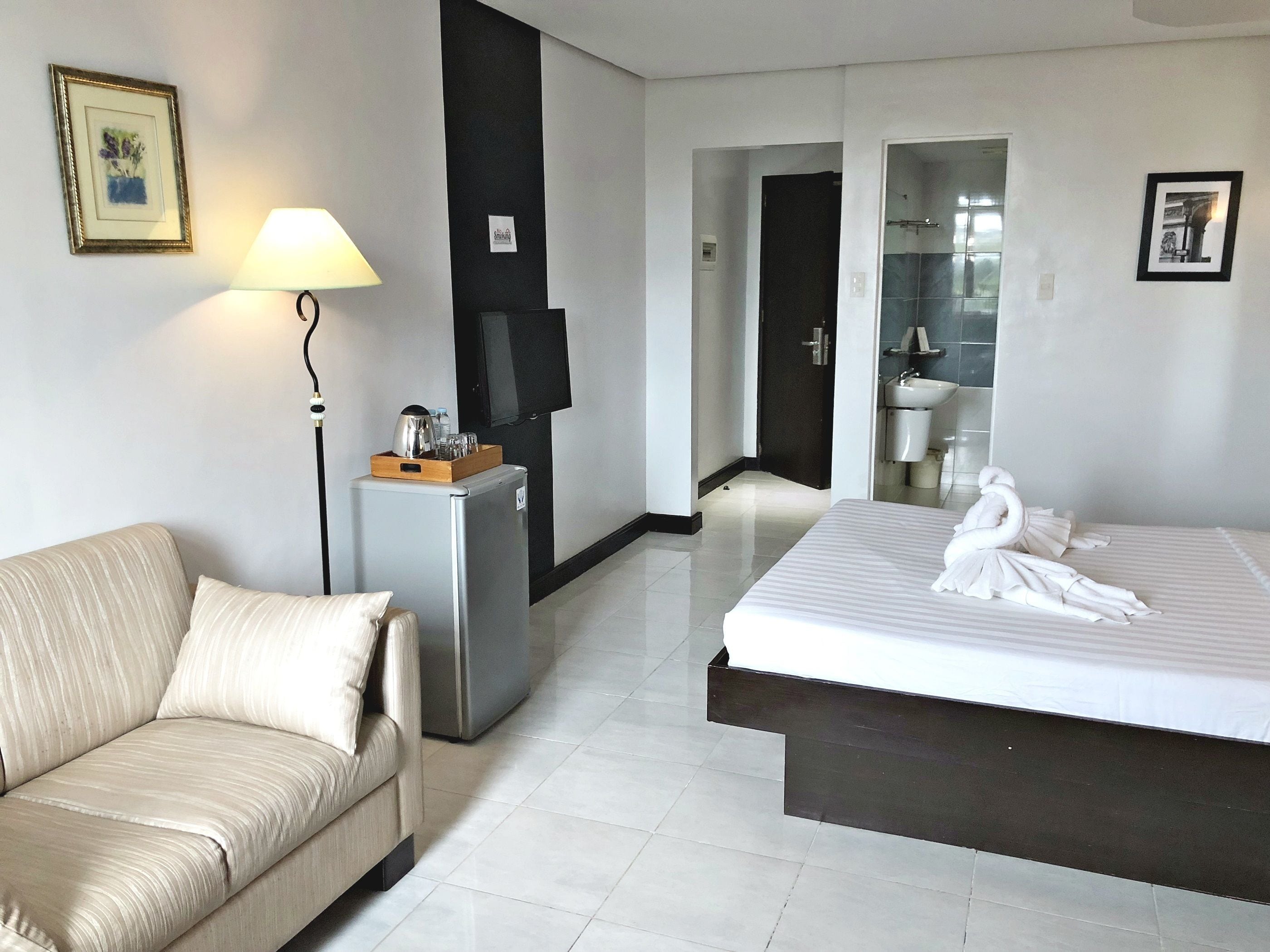 Habitación de hotel con cama, sofá, escritorio con lámpara, televisor y refrigerador.