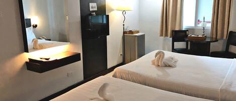 Habitación de hotel con dos camas, un escritorio, una silla, televisor, espejo y ventana con cortinas.