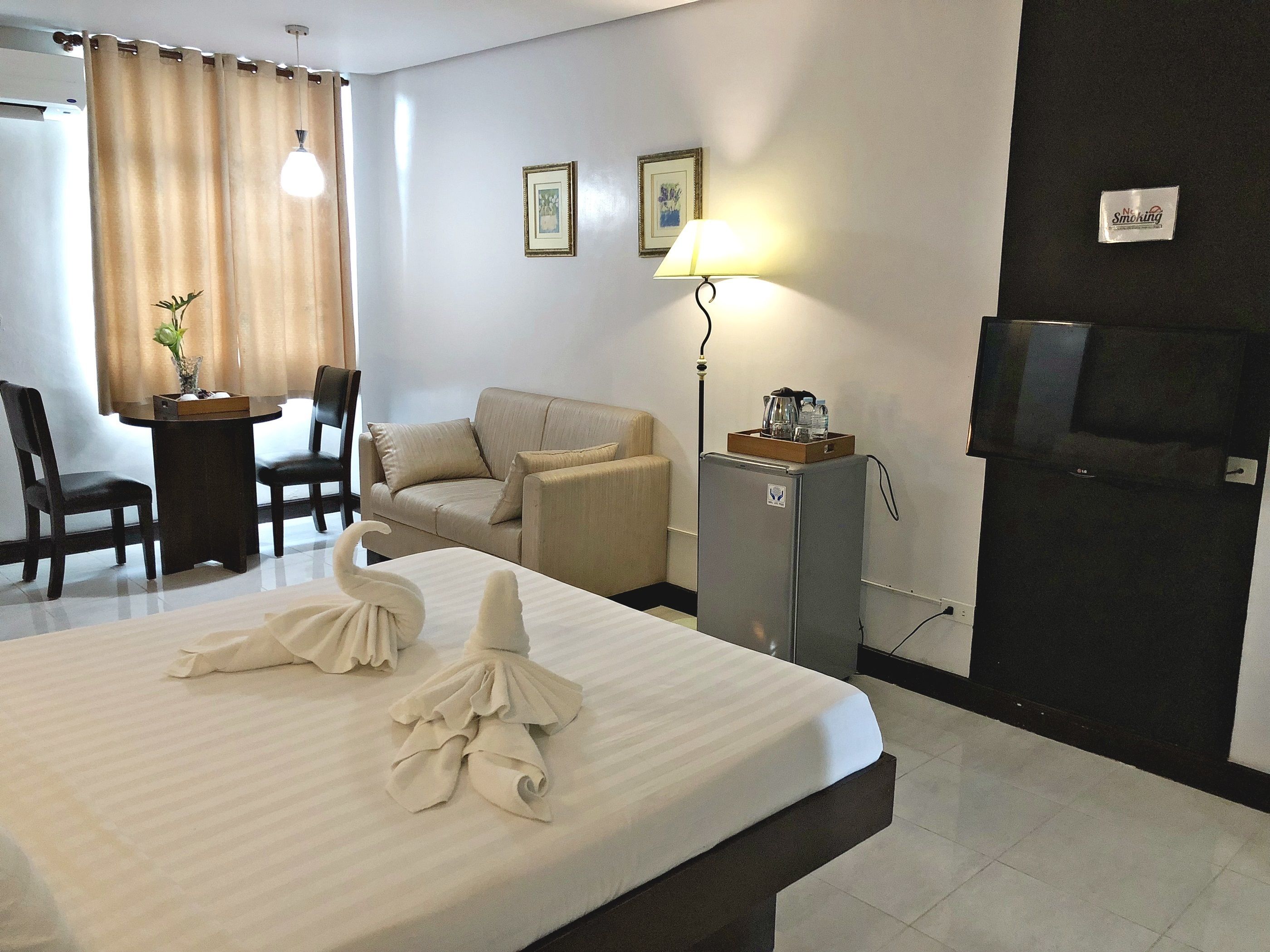 A hotel room with a bed, a desk, a chair, a sofa, a television, and a refrigerator.