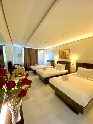 Habitación de hotel con dos camas, un escritorio, una silla, un florero con rosas rojas y un cuadro en la pared.