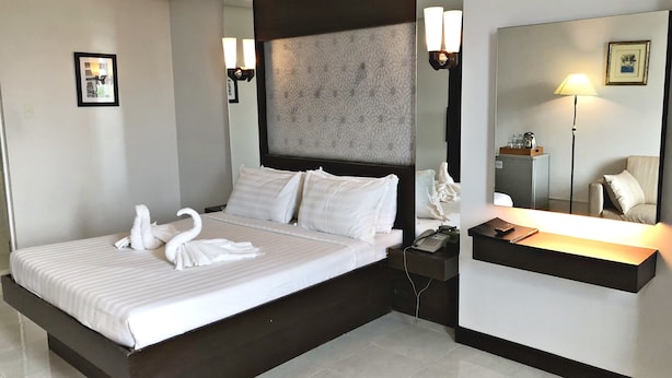 Habitación de hotel con una cama grande, una mesita de noche, un escritorio, una silla, un espejo y una lámpara de pared.