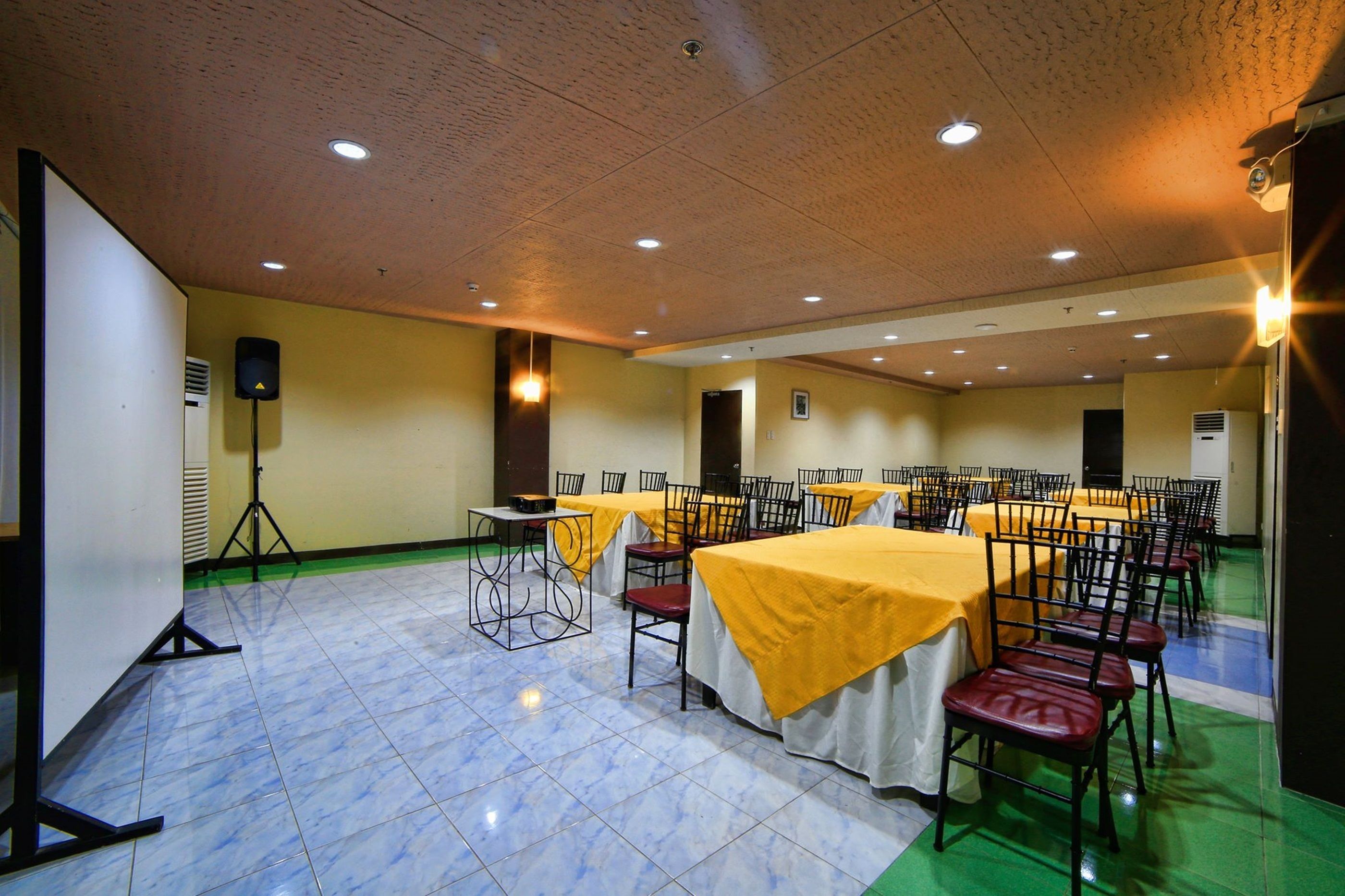 A conference room with multiple tables and chairs, equipped with a projector and speaker, and a green carpeted floor.