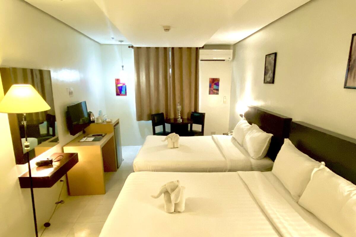 A hotel room with two beds, a desk with a computer, a lamp, and a television.