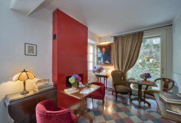 Une pièce avec un mur d’accent rouge, un sol à carreaux, un bureau avec des livres et une lampe, une chaise et une fenêtre avec des rideaux.