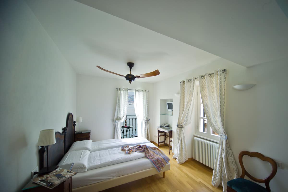 Une chambre à coucher avec un lit, un bureau, une chaise, un ventilateur de plafond et des rideaux.