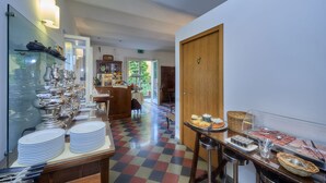Vestíbulo de hotel con piso a cuadros, zona de bufé con diferentes alimentos, y exhibición de cubiertos y platos.