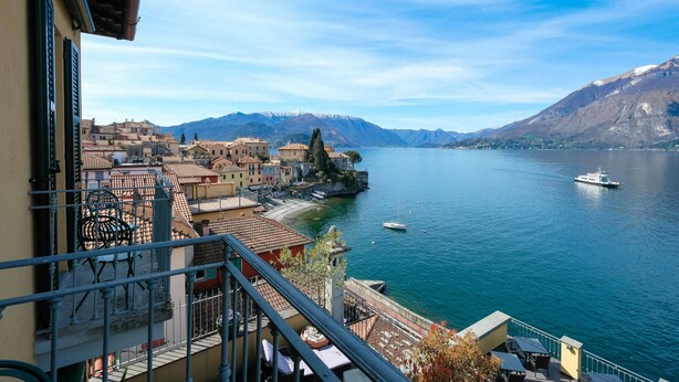 Un balcón con vistas a un lago, barcos y una cordillera.