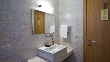 A bathroom with a tiled wall, a sink, a mirror, a wooden door, and a white toilet.
