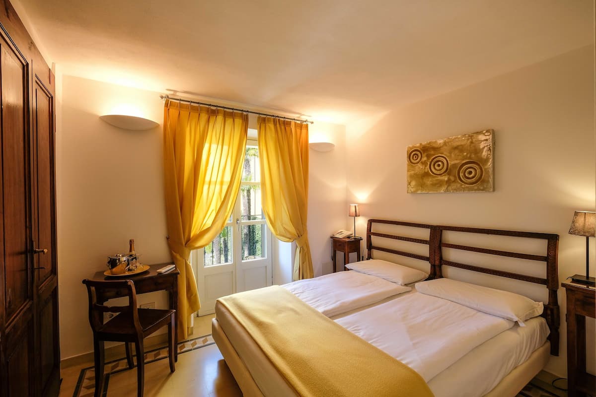 Une chambre avec deux lits, un bureau, une chaise, une lampe et une fenêtre avec des rideaux.