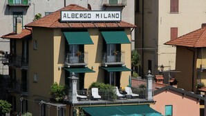 Un edificio con un letrero que dice "Albergo Milano" y terraza exterior con sombrillas.